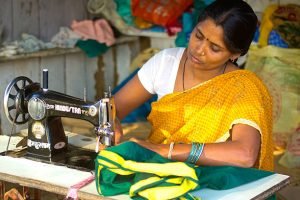 Bandhavgarh, India - January 8, 2014: Woman sewing sari, ladies cloth. In front of her is sewing machine and cloth, while in background there are shop materials.